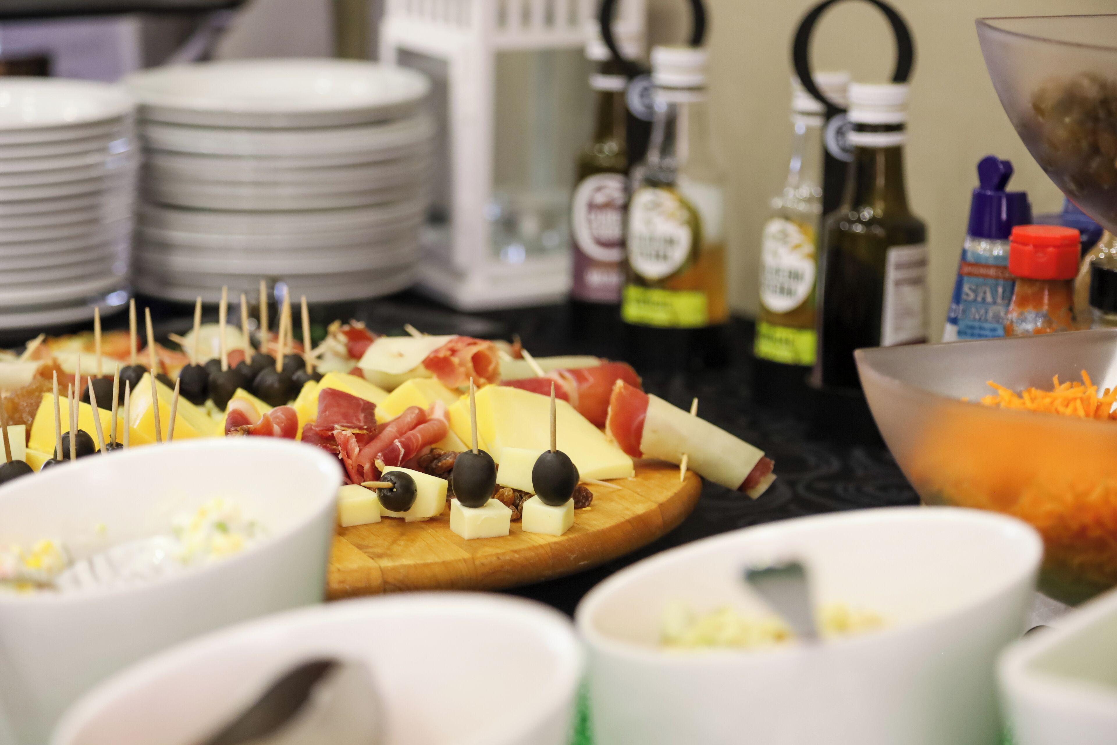 A buffet table with various food items, including cheese, olives, and meats, along with several condiment bottles.