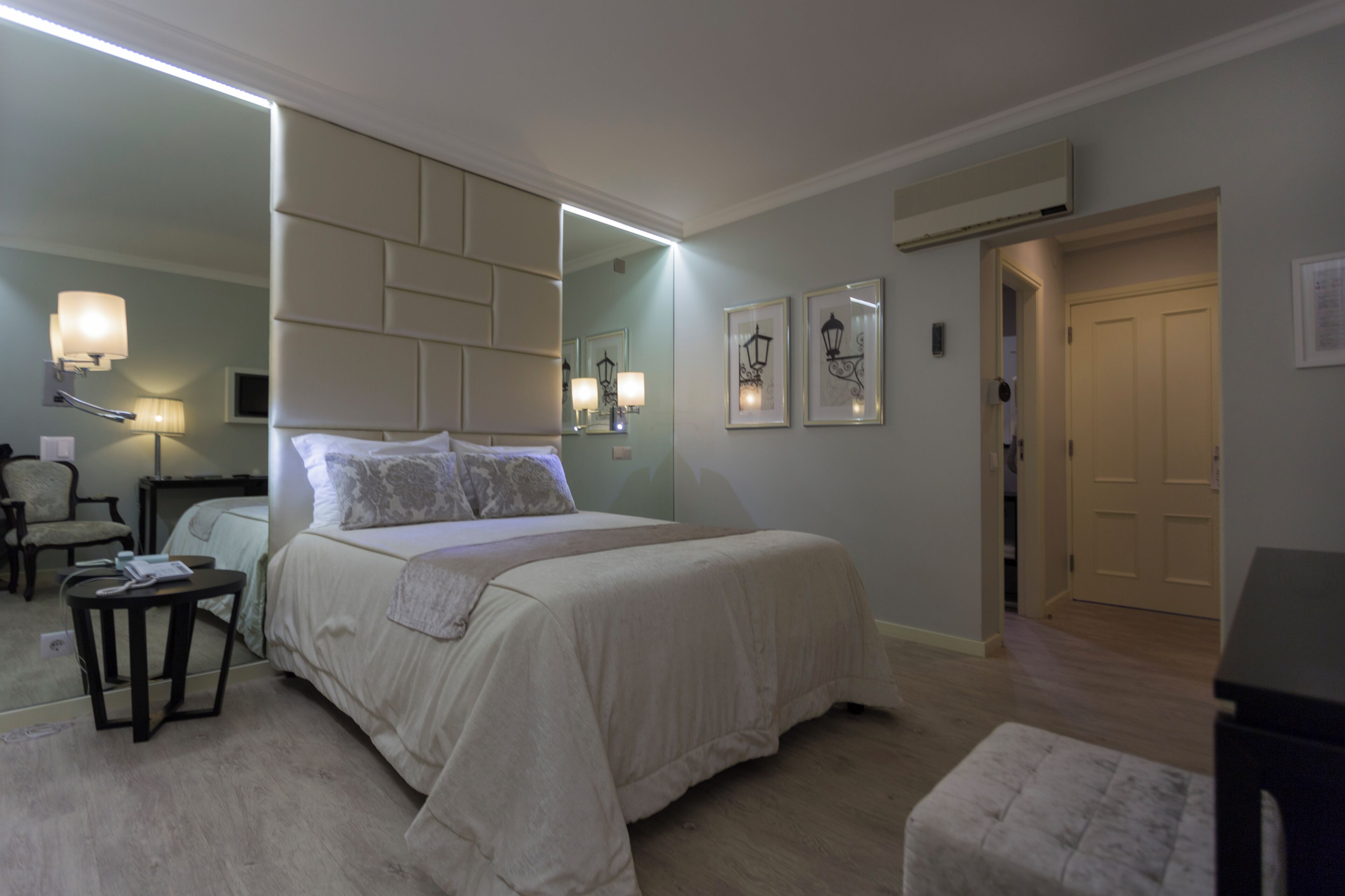 Habitación de hotel con una cama grande, una mesita de noche, una silla, un espejo y una puerta.