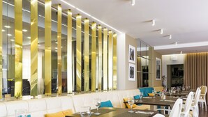 A restaurant with white leather seating, tables set with wine glasses, and a decorative wall with vertical golden elements. - Josefa D'Óbidos (Obidos)
