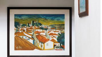 A framed painting of a coastal town with white buildings and red roofs, set against a blue sky.