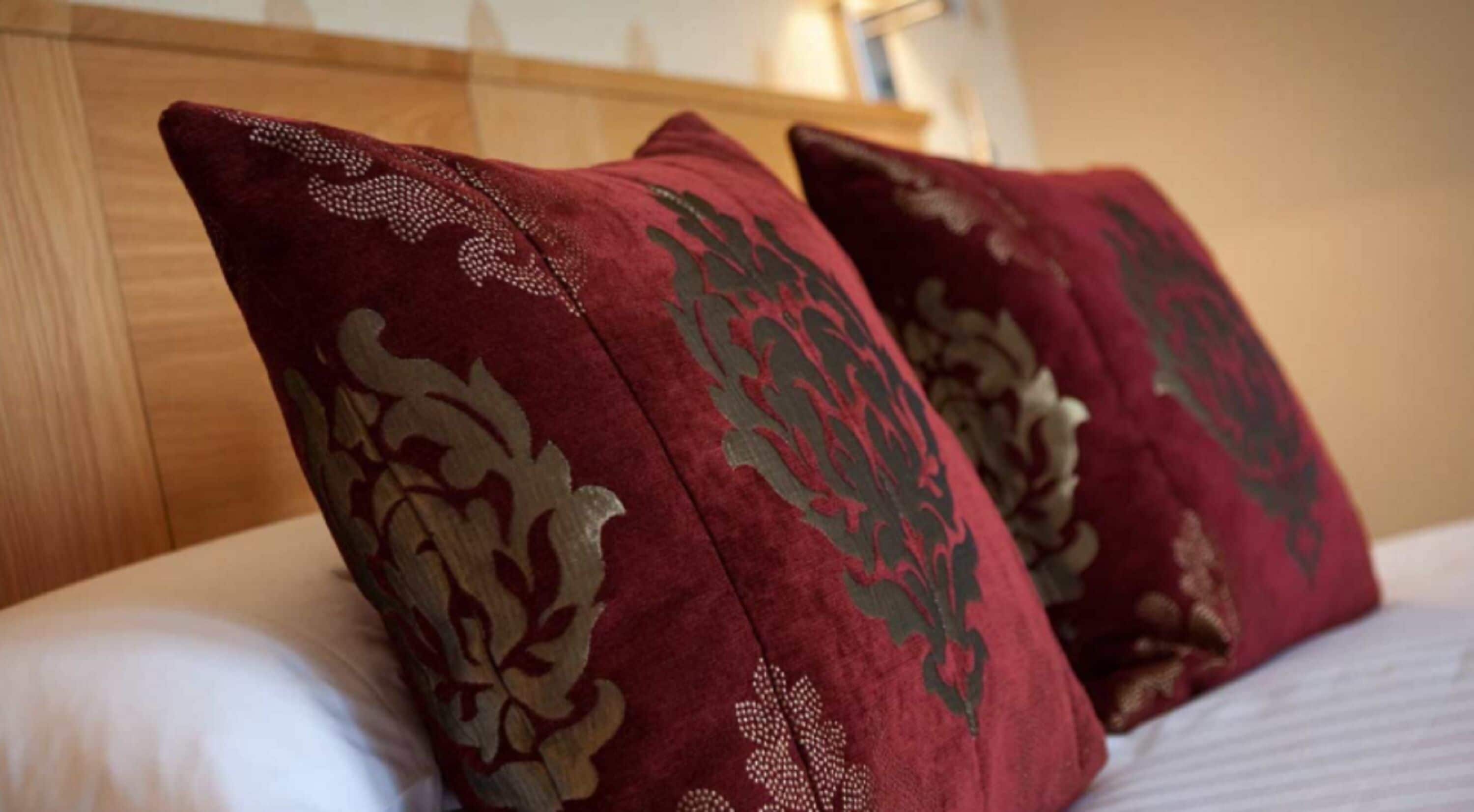 A bed with white linens and two red pillows with gold floral patterns.