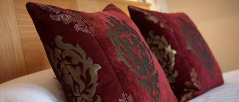Una cama con sábanas blancas y dos almohadas rojas con motivos florales dorados.