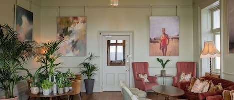 A spacious living room with a chandelier, multiple seating areas, and large paintings on the walls.