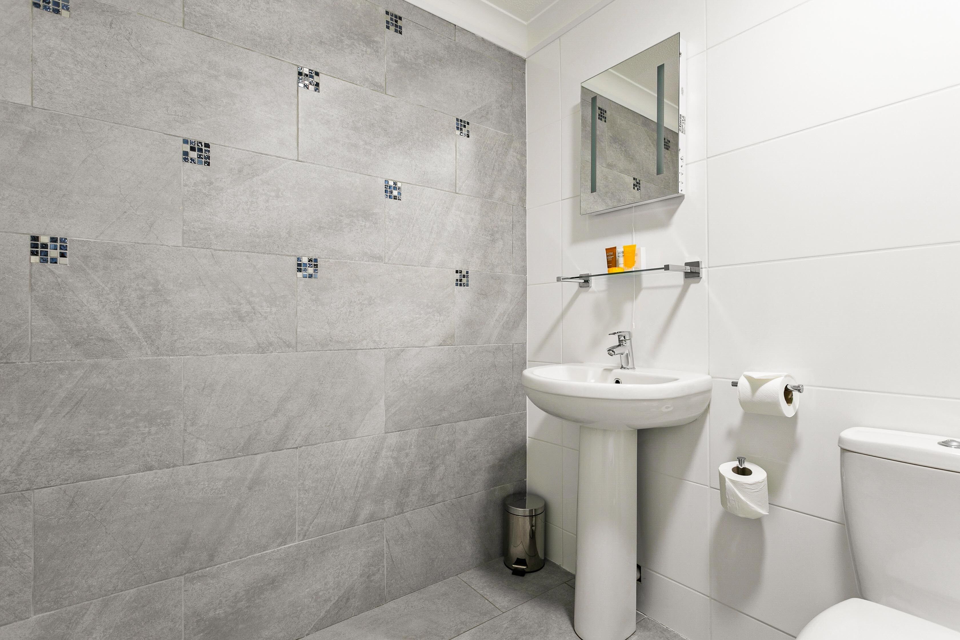 A modern bathroom with grey tiles, a white sink, a mirror, and a toilet.