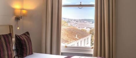 Una habitación de hotel con una cama grande, vistas a un paisaje urbano y una ventana con cortinas.