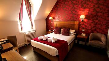 Ein Hotelzimmer mit einem großen Bett, zwei Nachttischen, einem Schreibtisch, einem Stuhl und einem fenster mit Vorhängen.