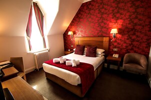 A hotel room with a large bed, two bedside tables, a desk, a chair, and a window with curtains.