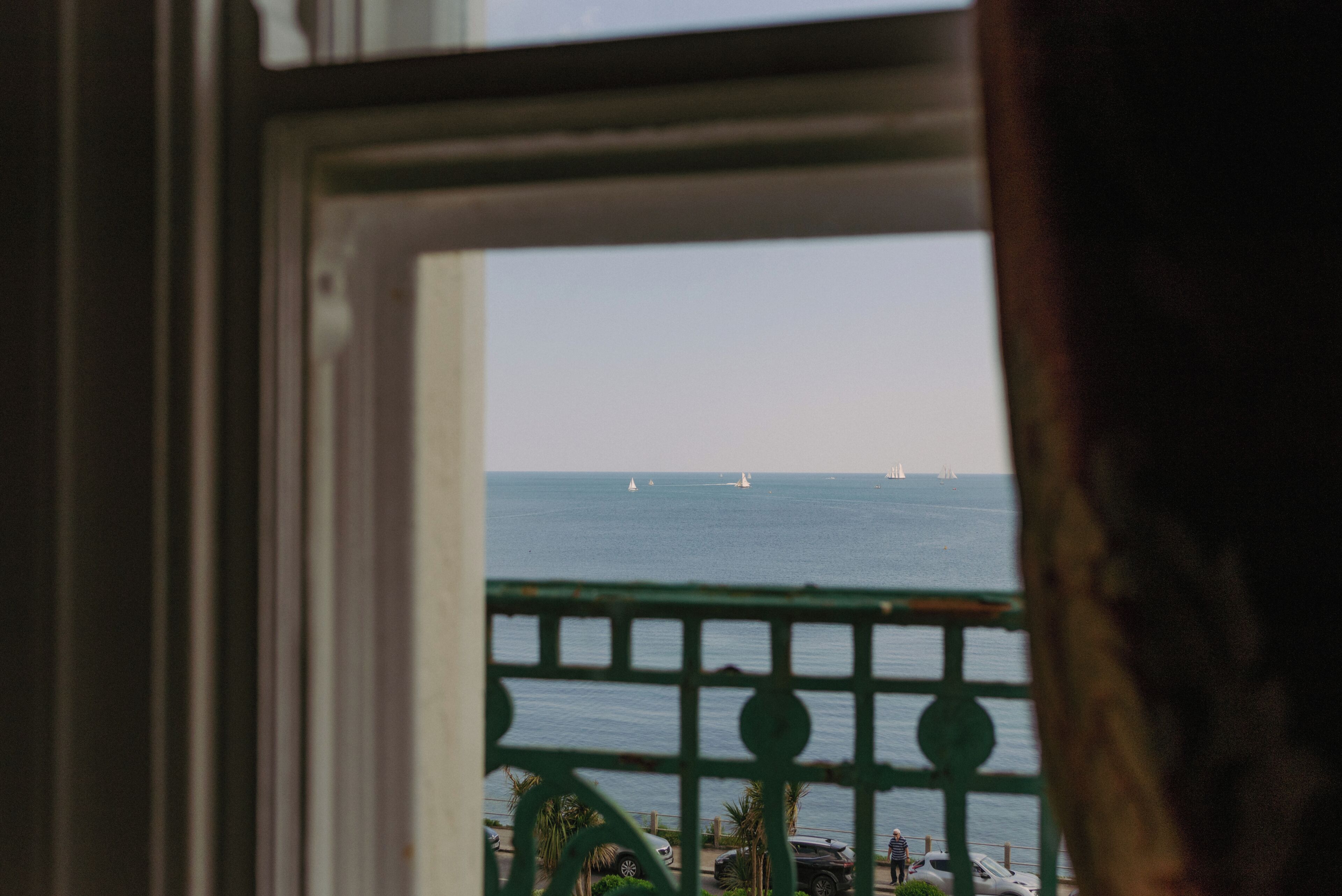 A view through a window with a metal railing, overlooking a body of water with sailboats.