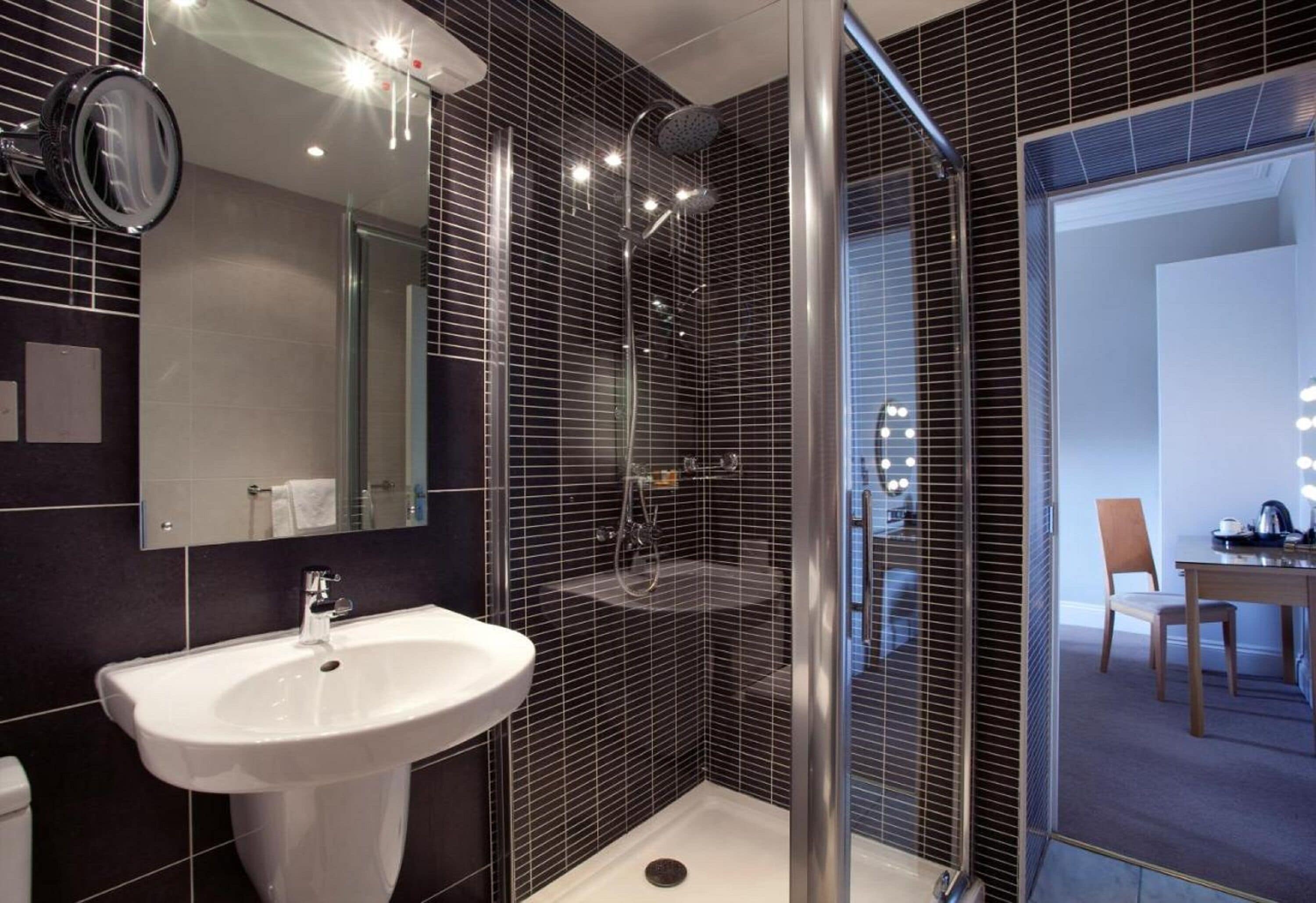 A modern bathroom with a white sink, a mirror, and a shower area.