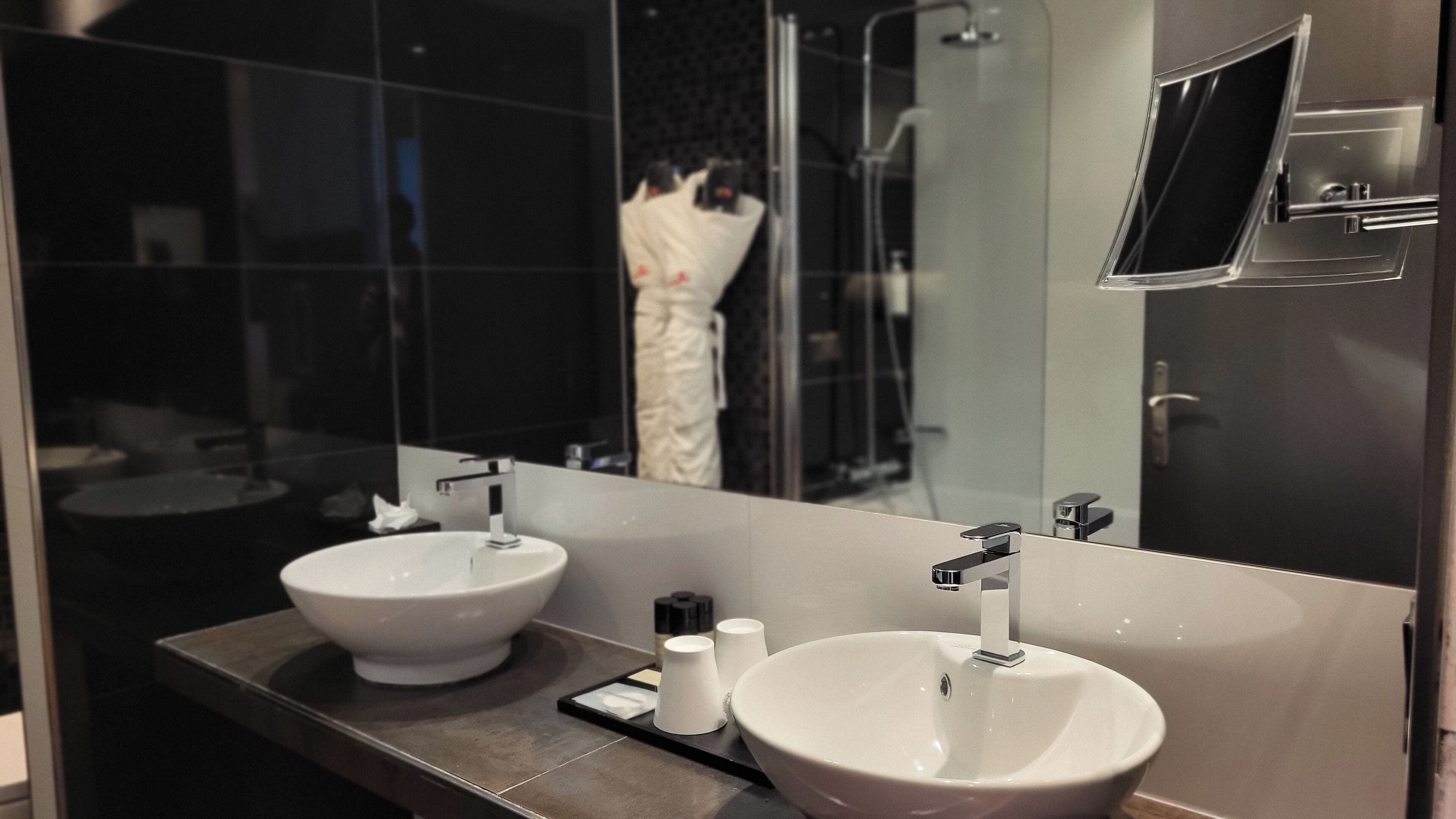 A modern bathroom with two sinks, a large mirror, and a shower area.