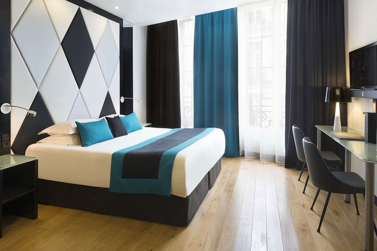 A modern hotel room with a bed, a desk, and chairs.