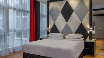 A modern hotel room with a large bed, a geometric wall design, and a view through sheer curtains.