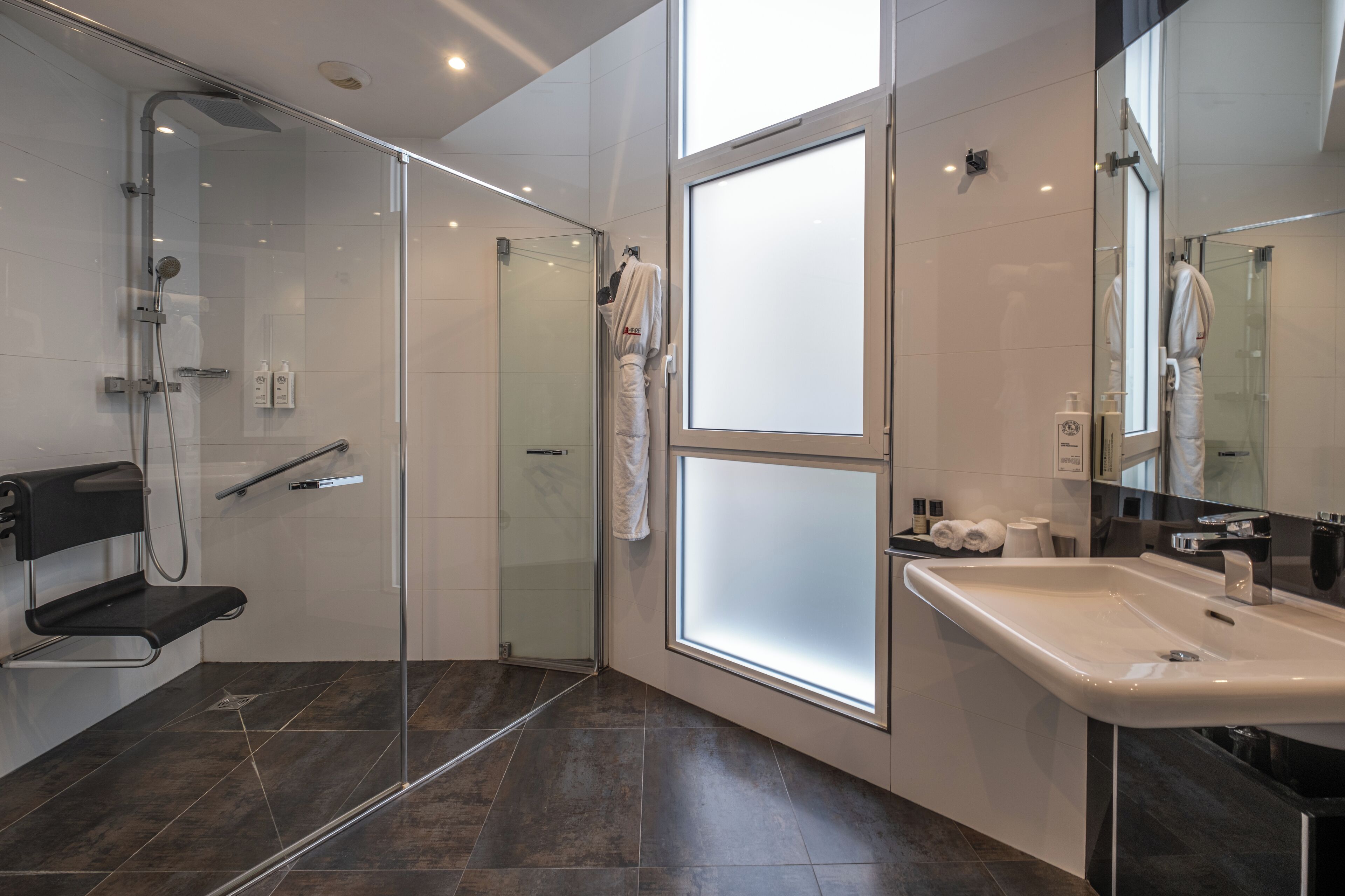 A modern bathroom with a glass-enclosed shower, a black bench, a large mirror, and a white sink.