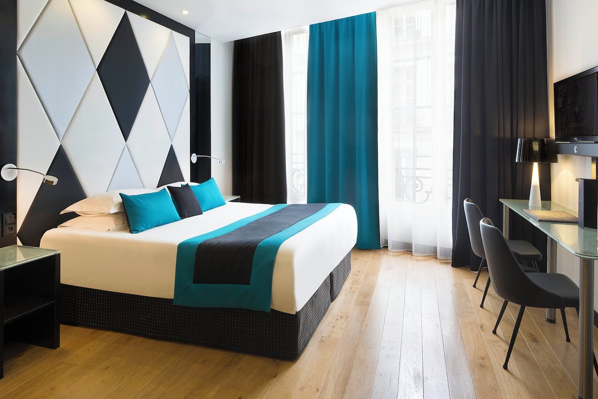 A modern hotel room with a large bed, a desk, and a TV.