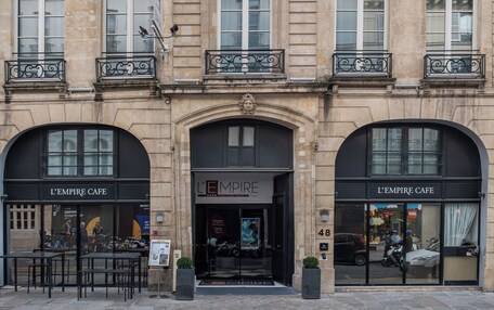 A building with multiple windows, a central entrance with a decorative arch, and two storefronts labeled "L'EMPIRE CAFE".
