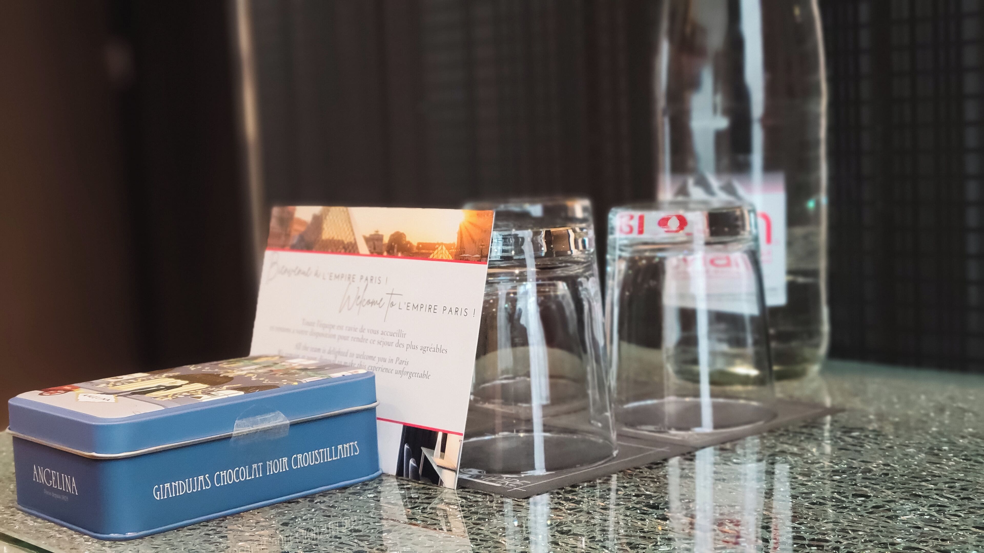 A glass display case with a sign, a blue box labeled 'Angelina Gianduja Chocolat Noir Crostillants', and a bottle with a red label.