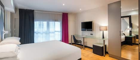 A modern hotel room with a large bed, a desk with a chair, a flat-screen TV, and a large mirror.