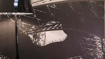 Una habitación con un gran mural de la Torre Eiffel, un sofá negro moderno y una mesita con una lámpara.