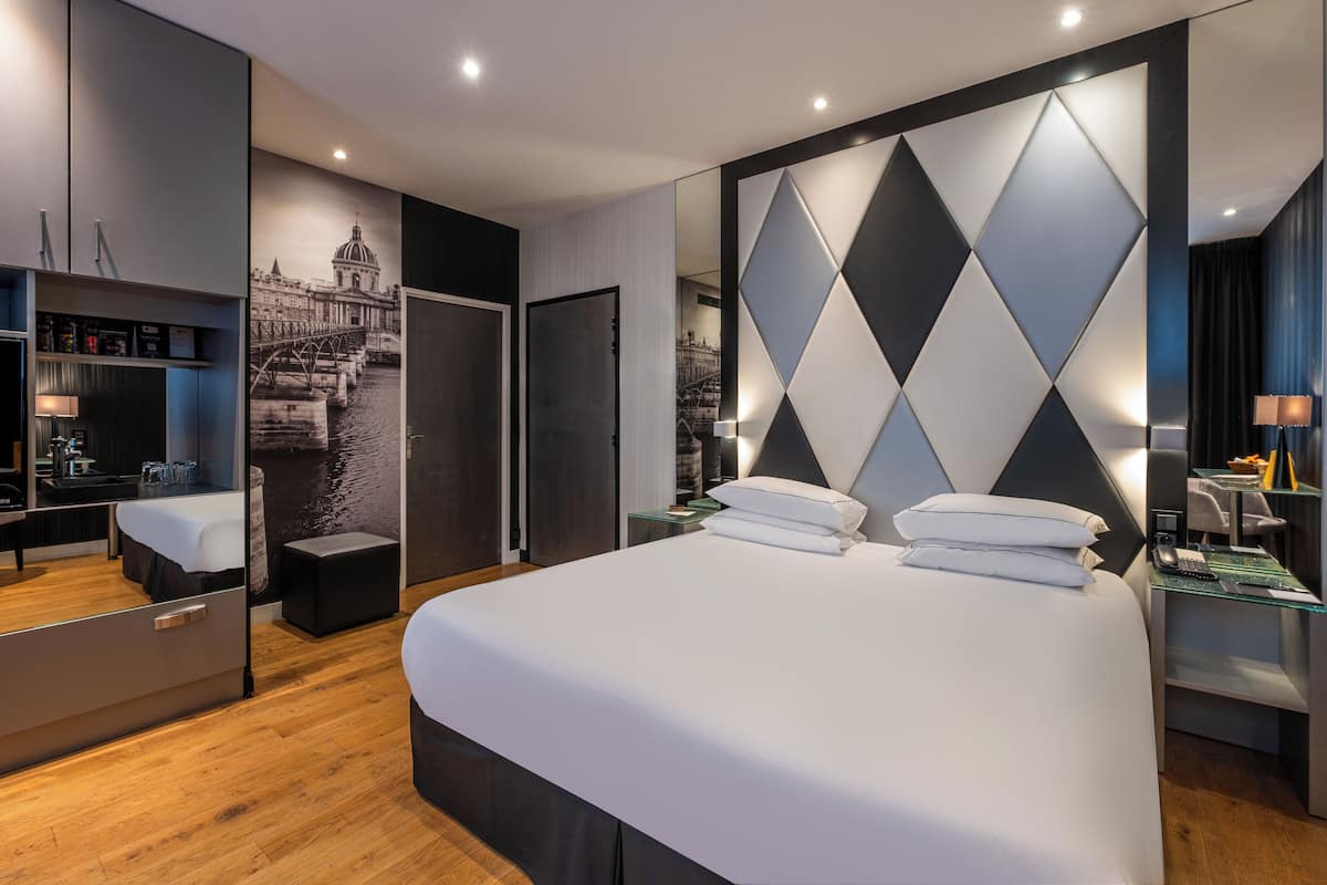 A modern hotel room with a large bed, a wardrobe, a desk with a lamp, and a wall-mounted TV.