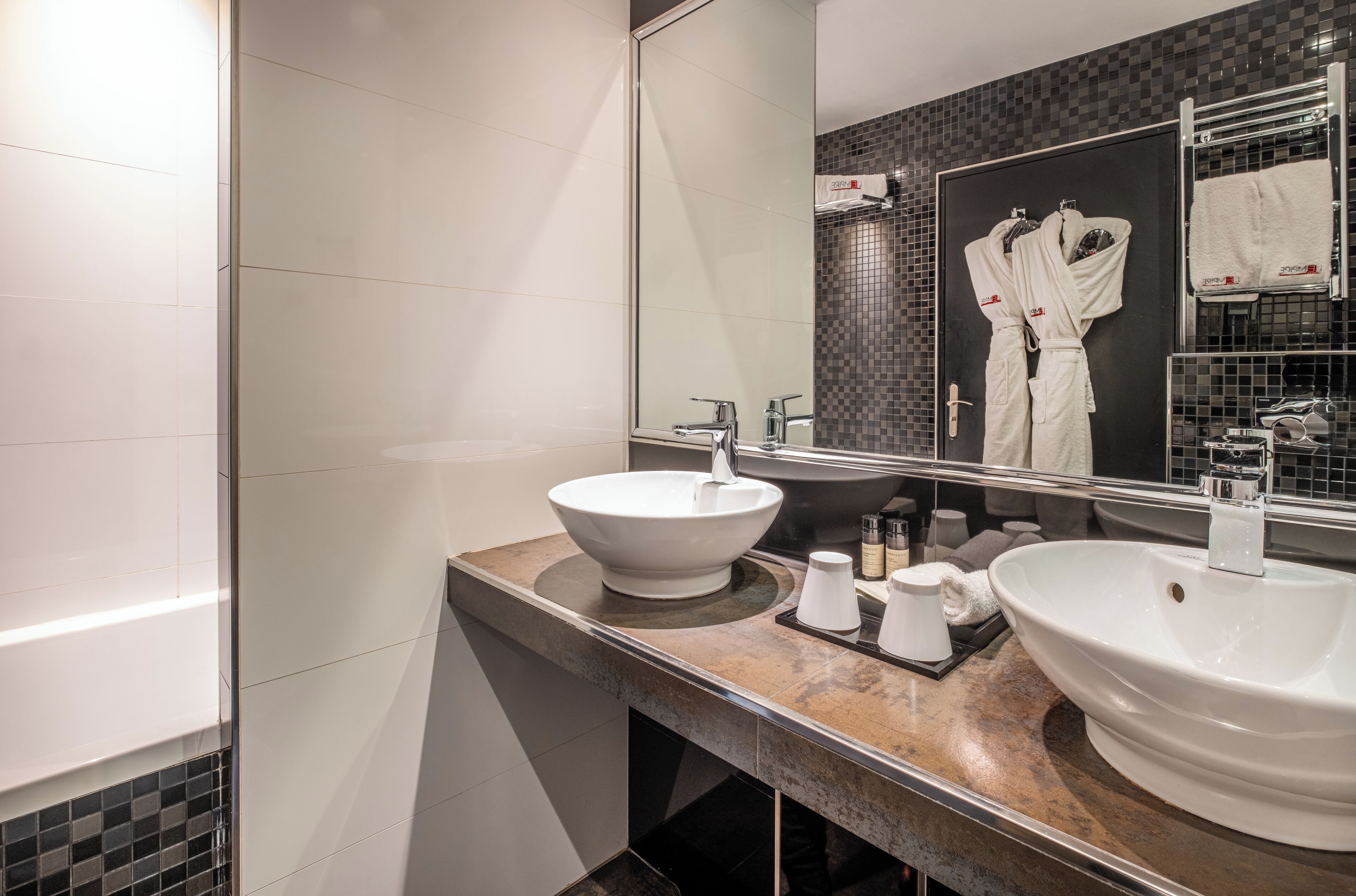 A modern bathroom with two sinks, a large mirror, and a towel rack with robes.