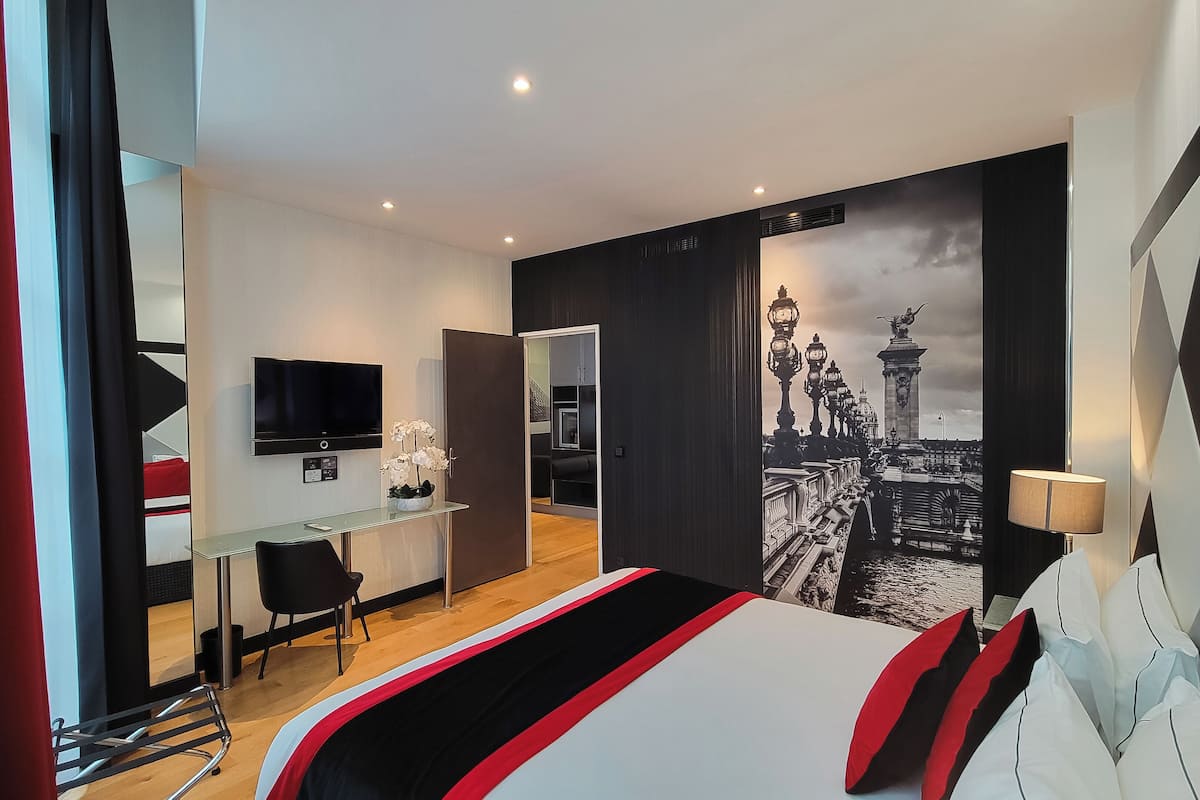 A modern hotel room with a bed, a desk, a TV, and a large cityscape wall.