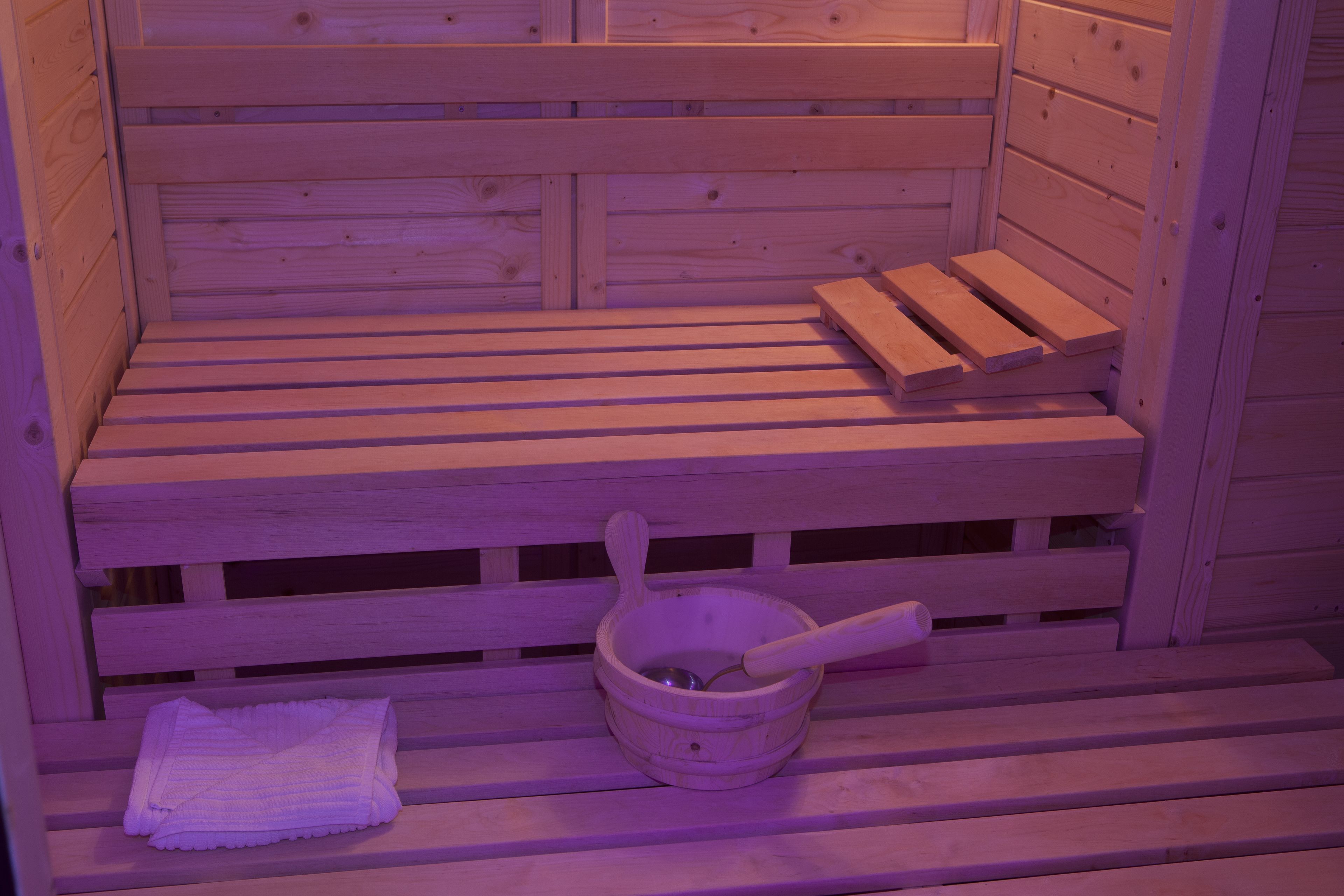 A wooden sauna bench with a wooden bucket and a towel.