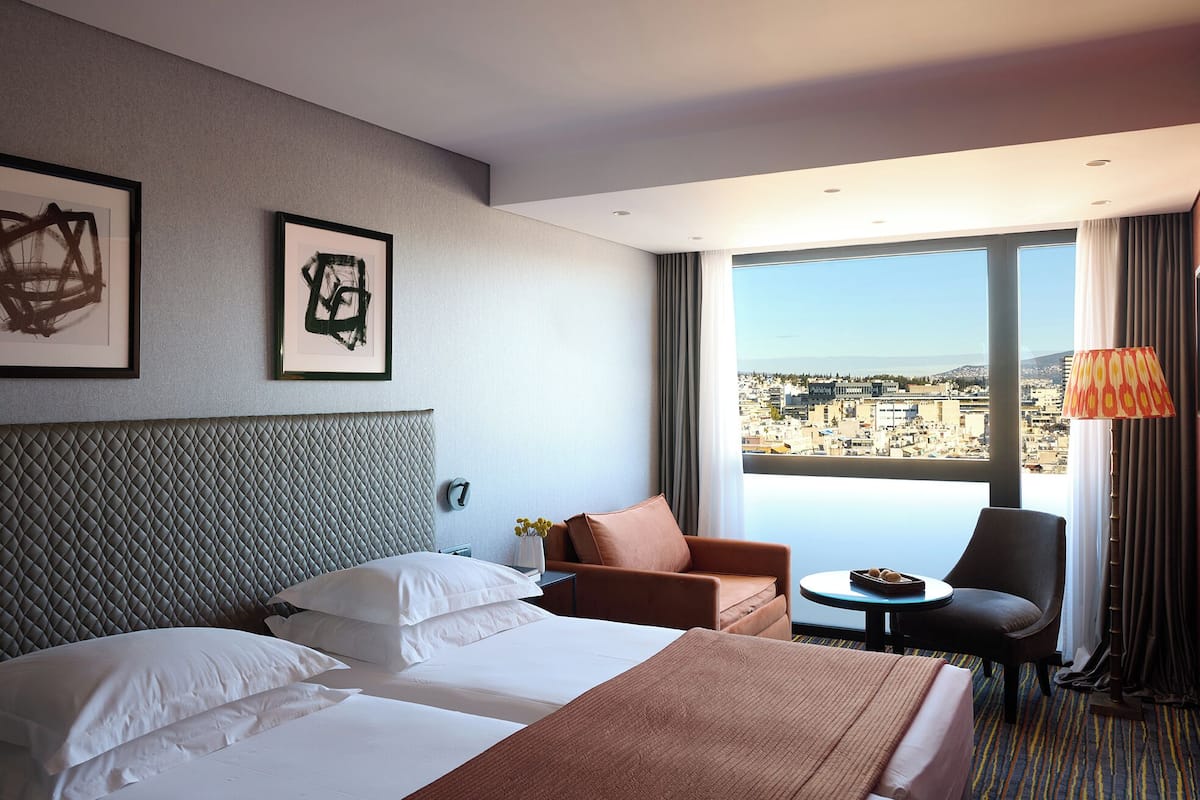 A hotel room with a large bed, a sofa, a chair, and a view of a cityscape.