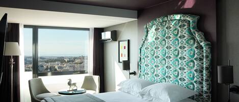 Habitación de hotel con una cama grande, una silla, un escritorio y vistas a la ciudad.