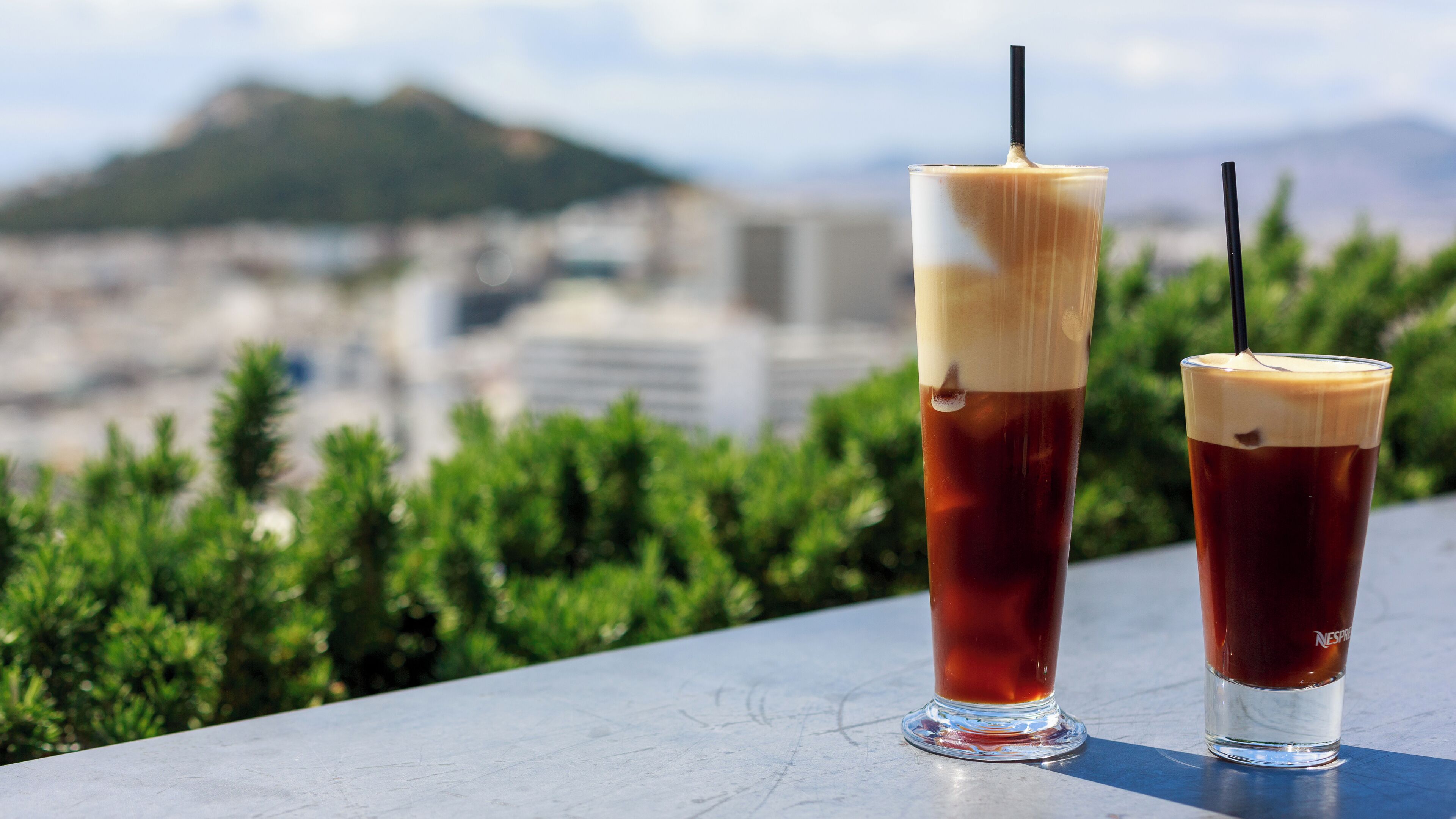 Dos cafés helados sobre una mesa, con vistas a un paisaje urbano de fondo.