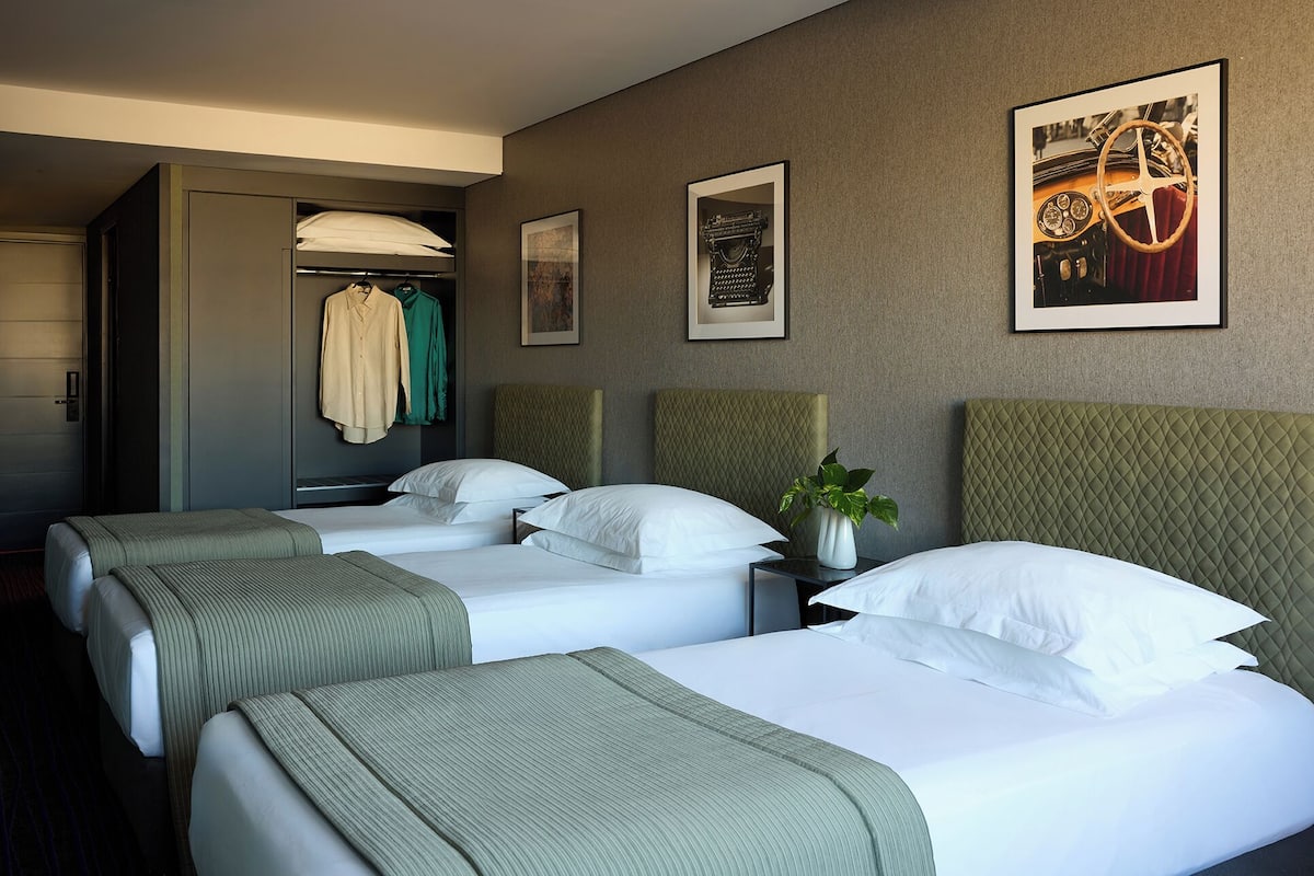 A hotel room with two beds, a wardrobe, and framed pictures on the wall.