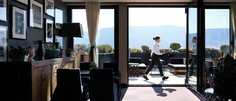 A modern hotel room with a large sliding glass door leading to an outdoor terrace with a mountain view.