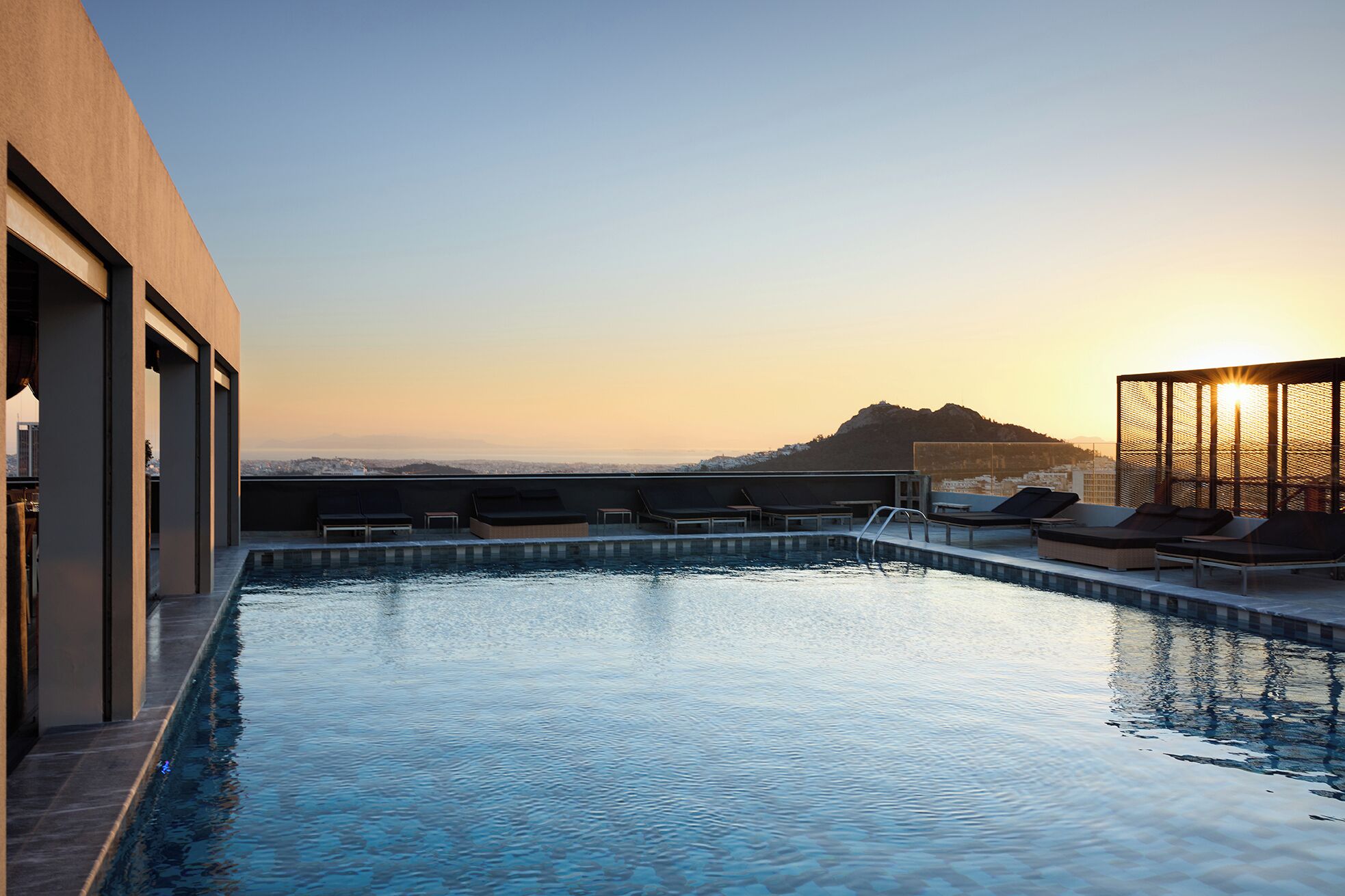 Piscina infinita en la azotea con sillones de descanso y vistas a una montaña al atardecer.