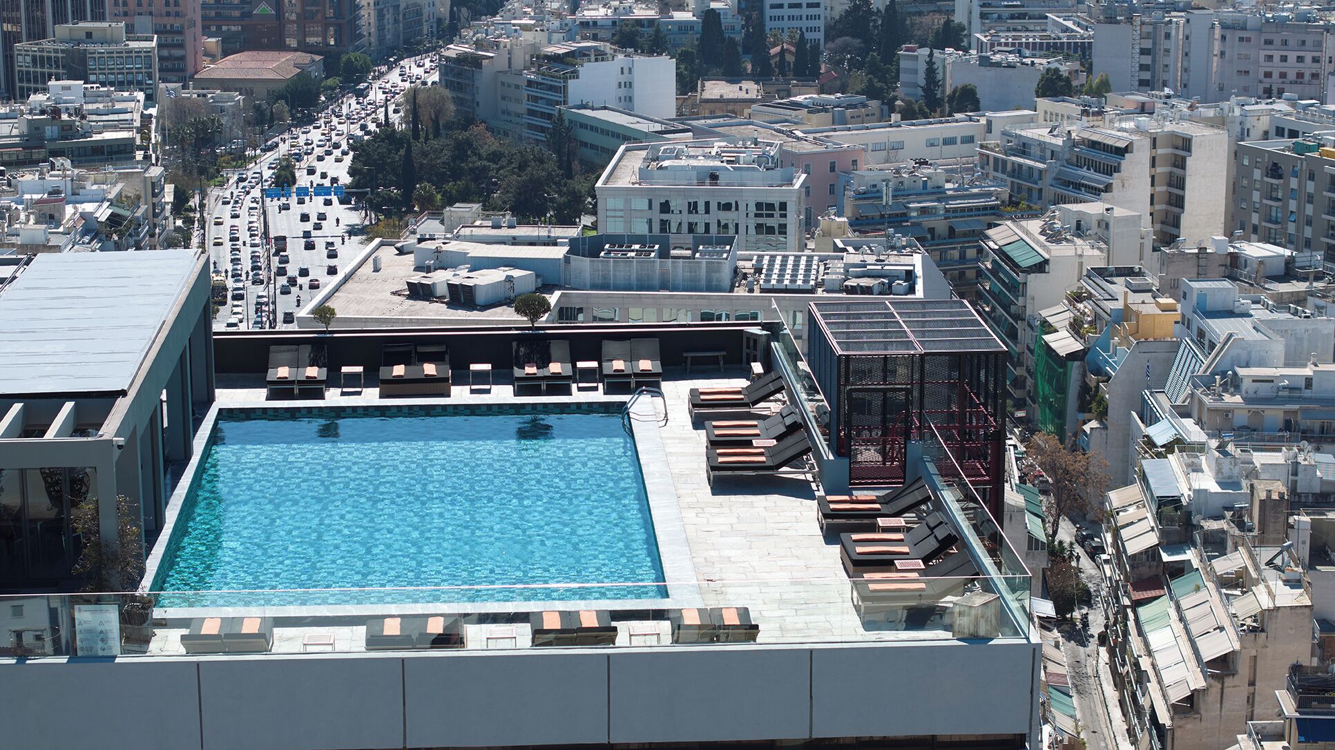 A rooftop pool with sun loungers and a view of the cityscape.