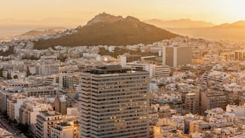Um hotel imponente com vários andares, situado em meio a uma área urbana densa, com diversos edifícios e uma colina imponente ao fundo.