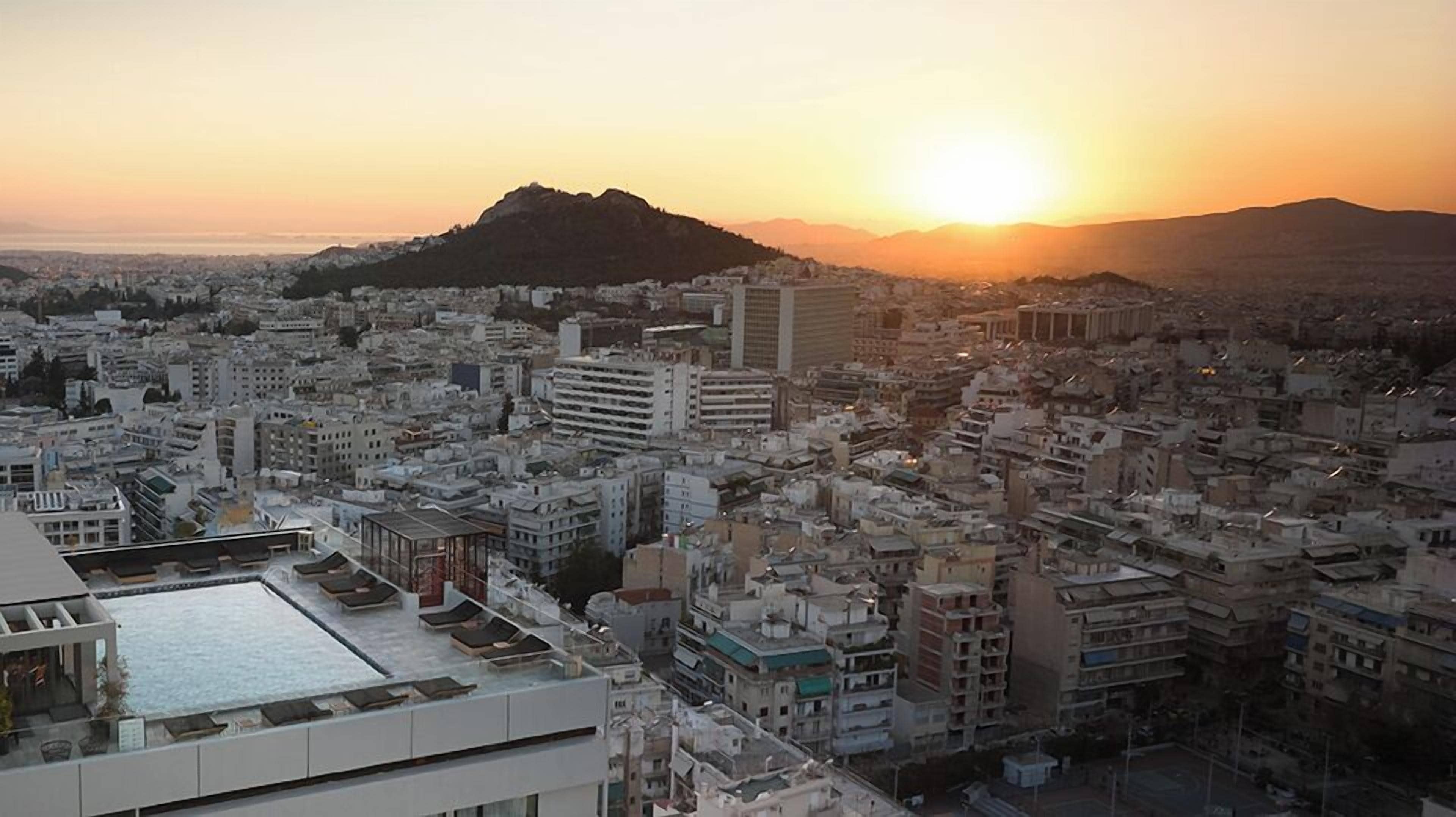 A cityscape with a large building featuring a rooftop terrace with sun loungers.