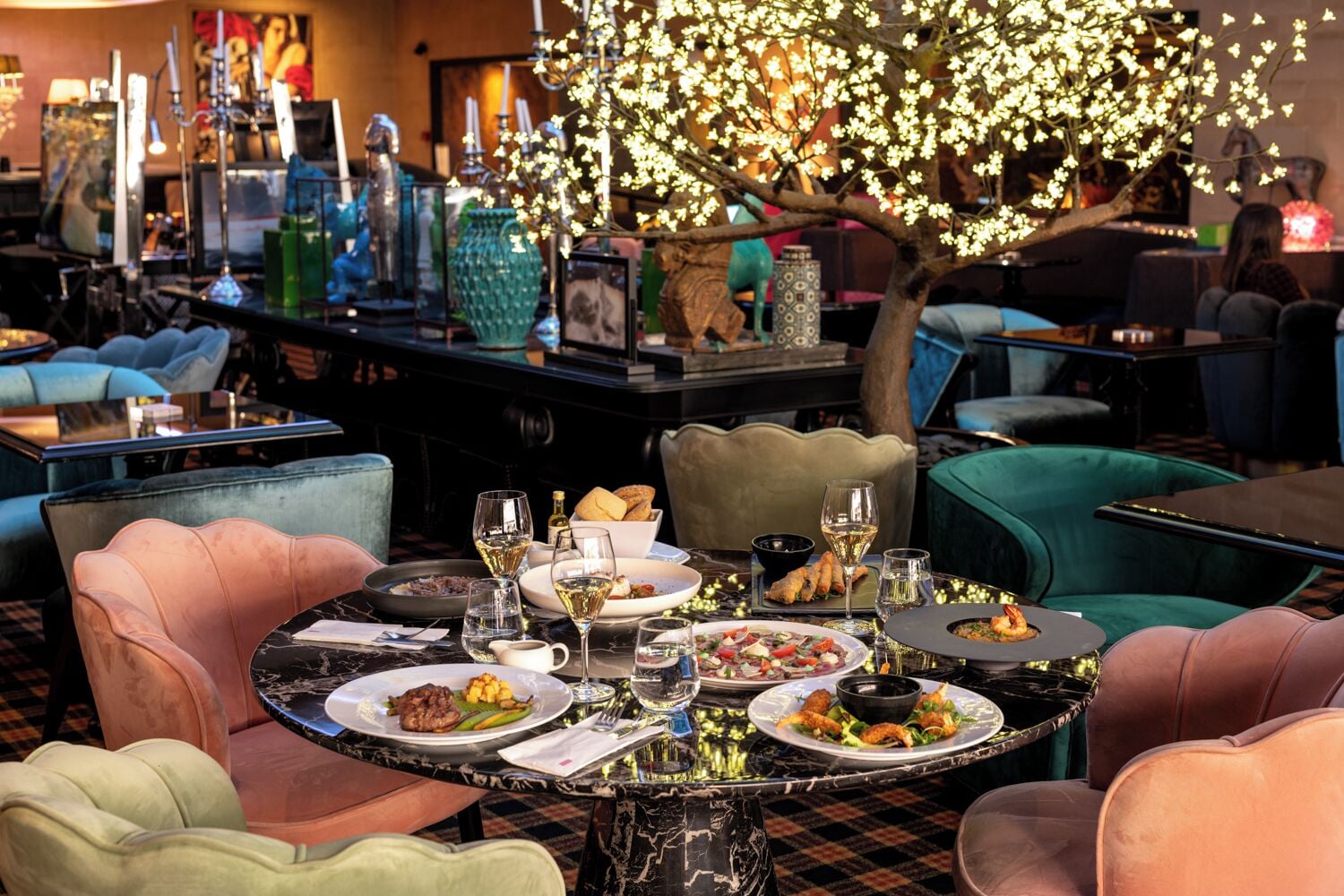 Un restaurant avec des tables et des chaises rondes, ainsi qu’un arbre décoratif illuminé.