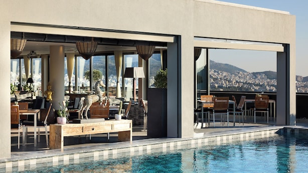 A modern poolside area with outdoor seating, a statue, and a view of a cityscape. - President Hotel Athens (Athens)