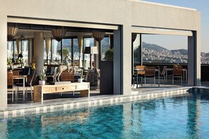 A modern poolside area with outdoor seating, a statue, and a view of a cityscape.