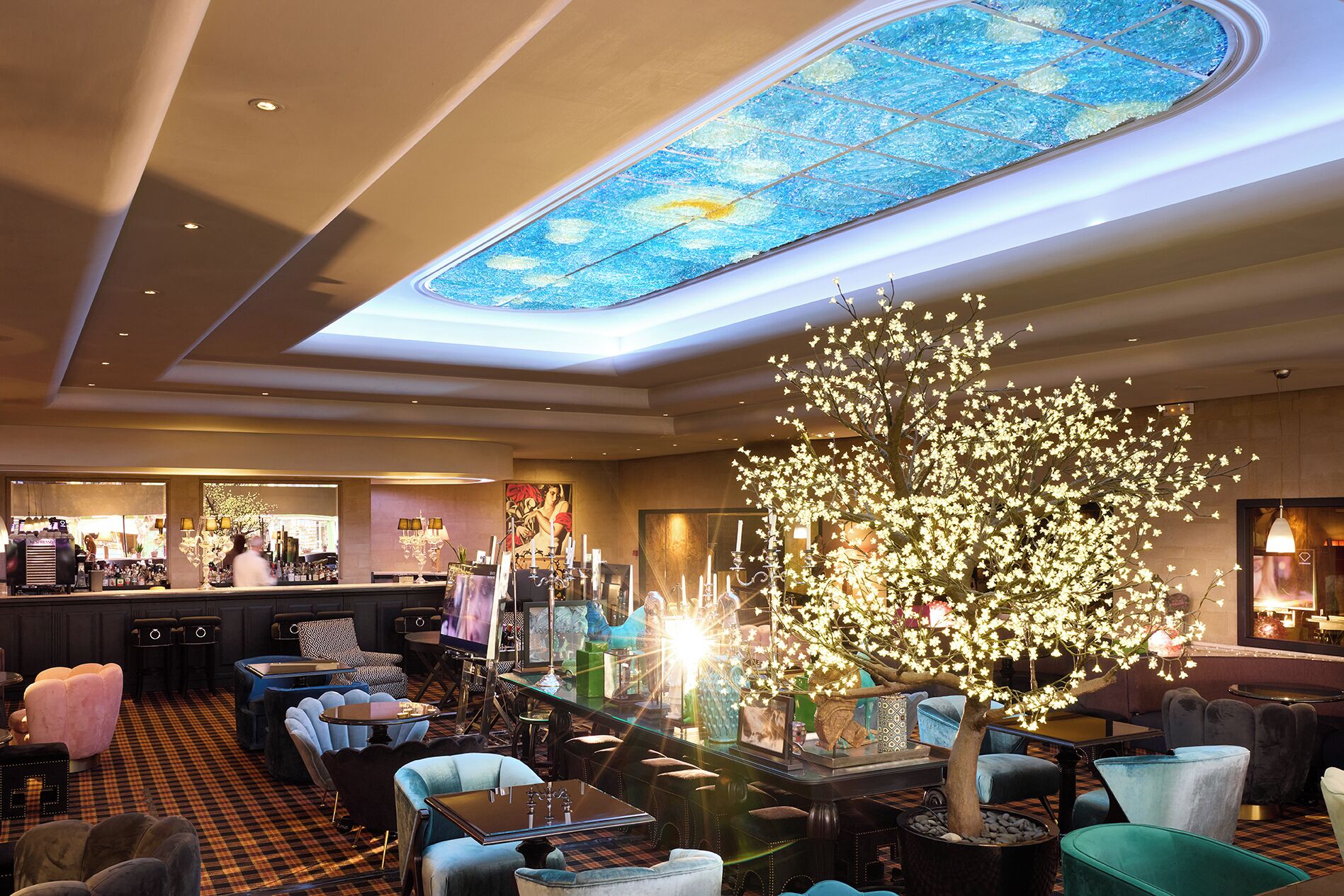 A hotel lobby with a large chandelier, seating area, and a decorative tree.