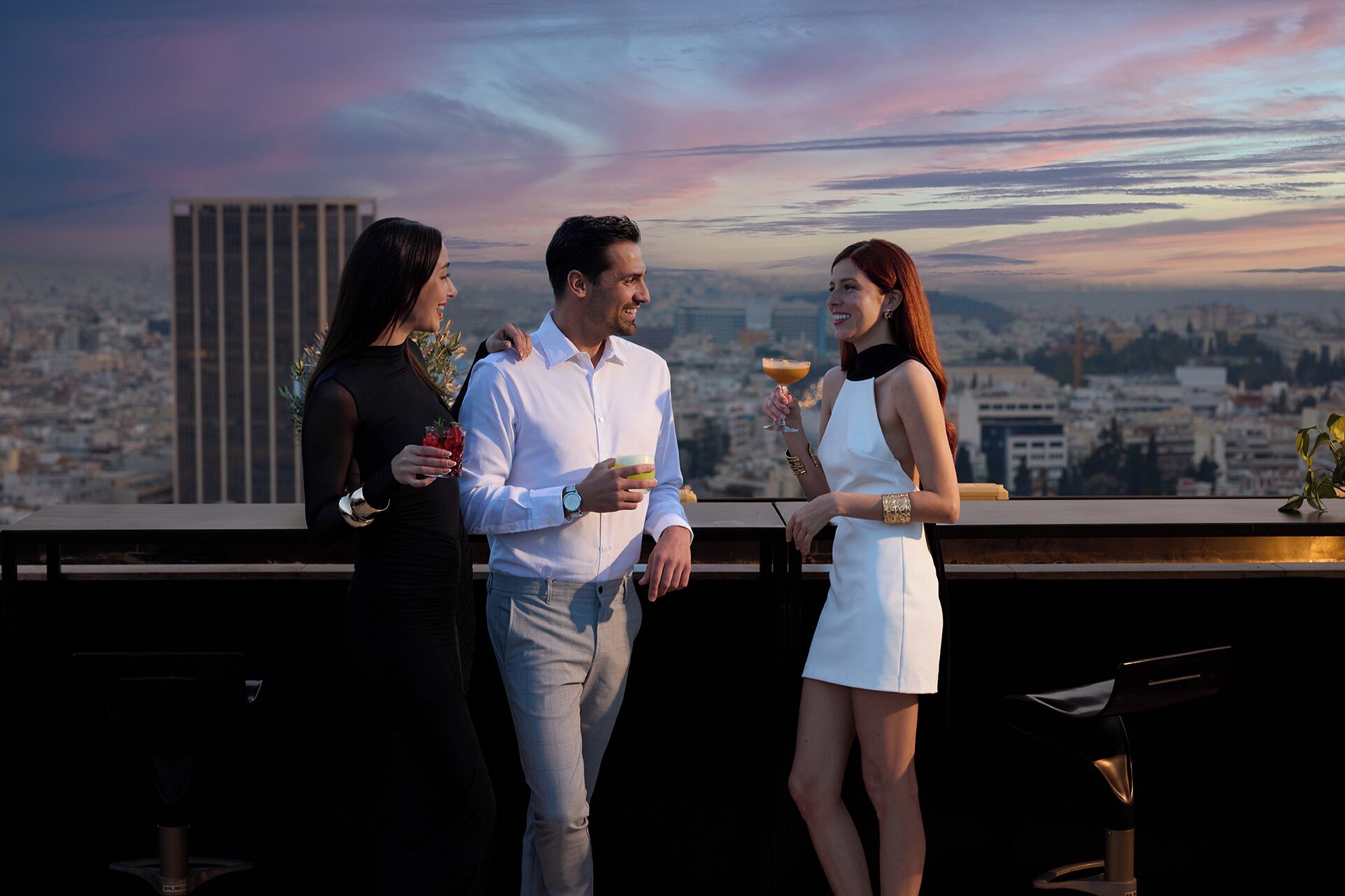 Three people standing on a rooftop terrace with a cityscape view.