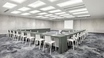 Una sala de conferencias con una larga mesa, sillas blancas y piso alfombrado.