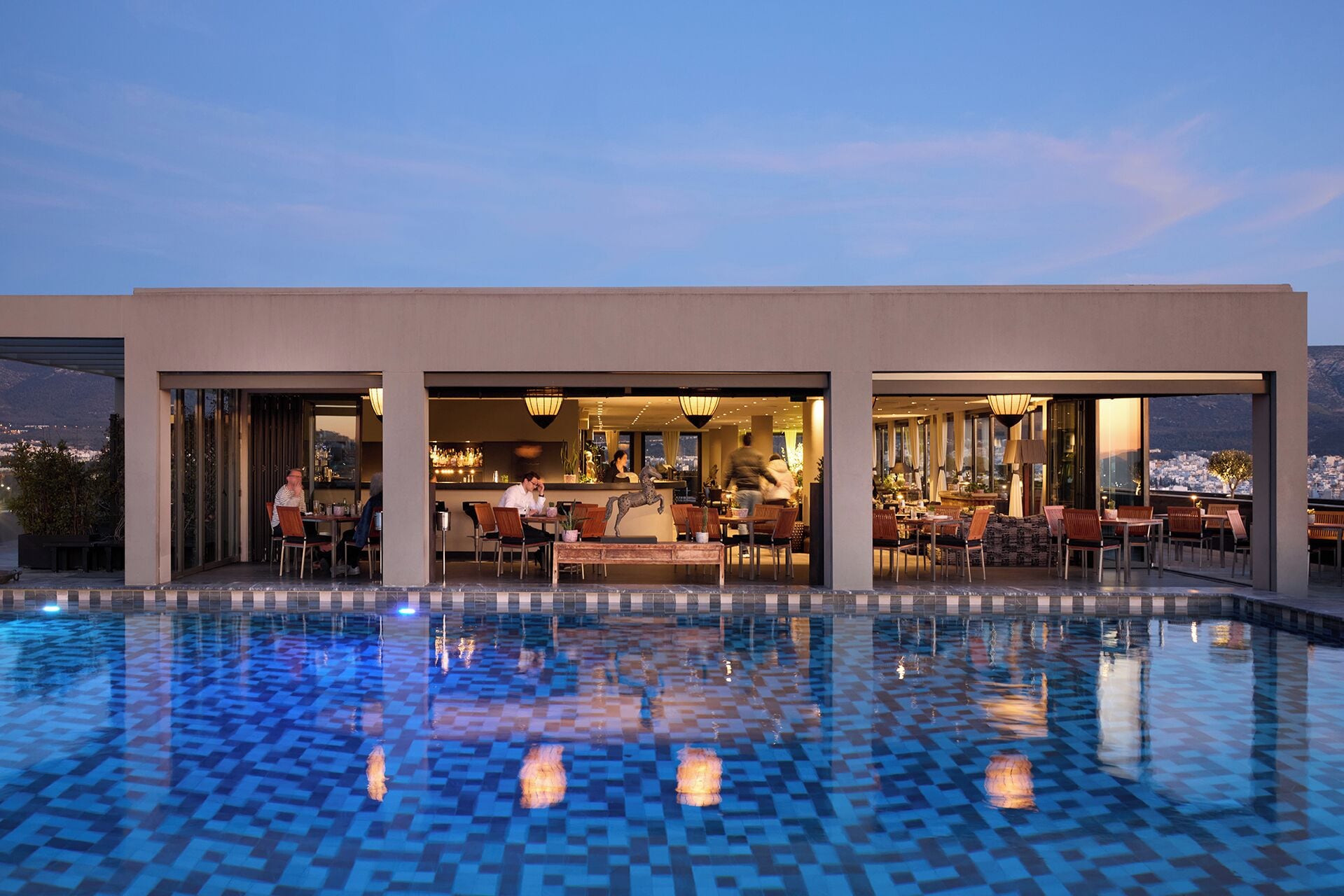 Un hotel modern amb una piscina exterior, una zona de bar i espais per seure.