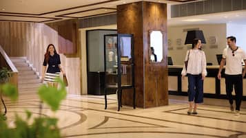 A lobby with a grand staircase, a reception desk, and a decorative column.