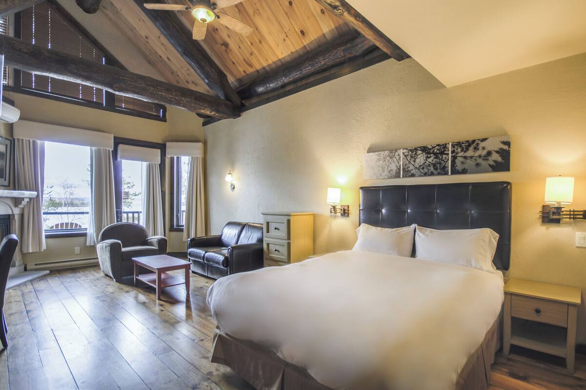 A hotel room with a large bed, a wooden ceiling, a sofa, and a desk.