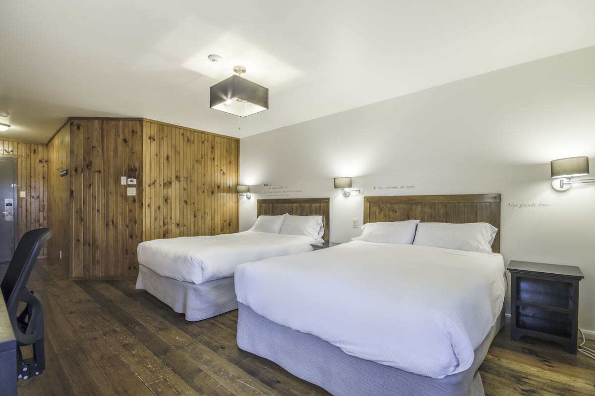 A hotel room with two beds, wooden paneling on the walls, and a desk with a chair.