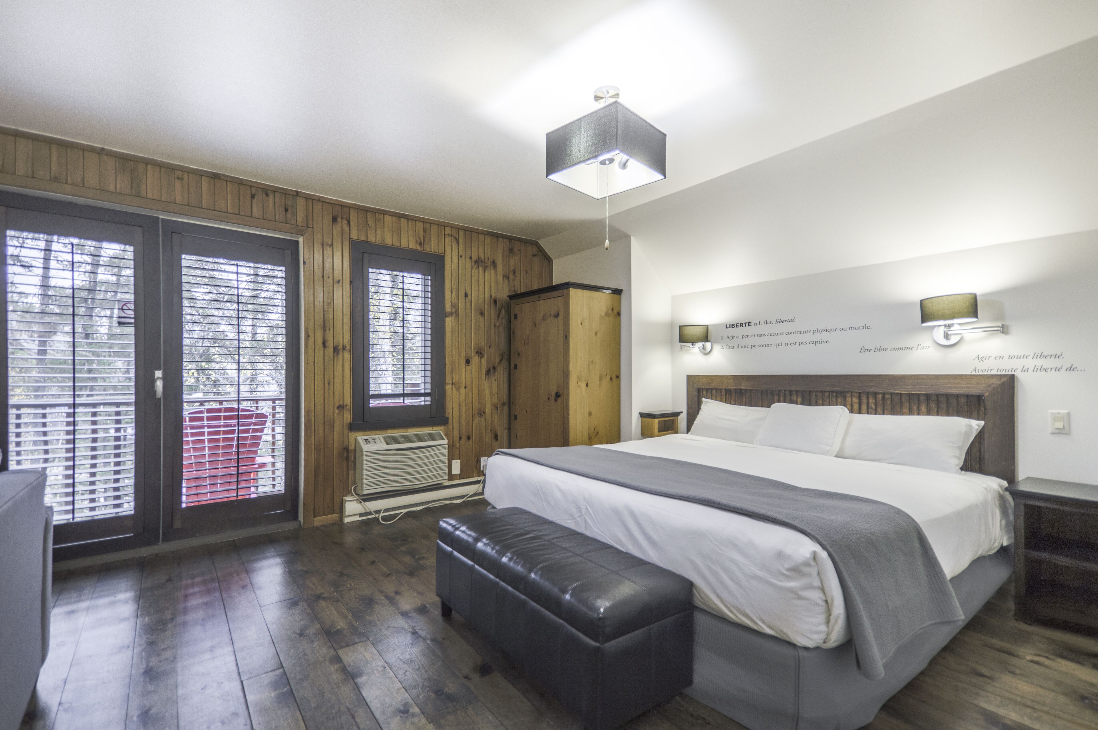 Een slaapkamer met een groot bed, houten wanden, een bankje en een plafondlamp.