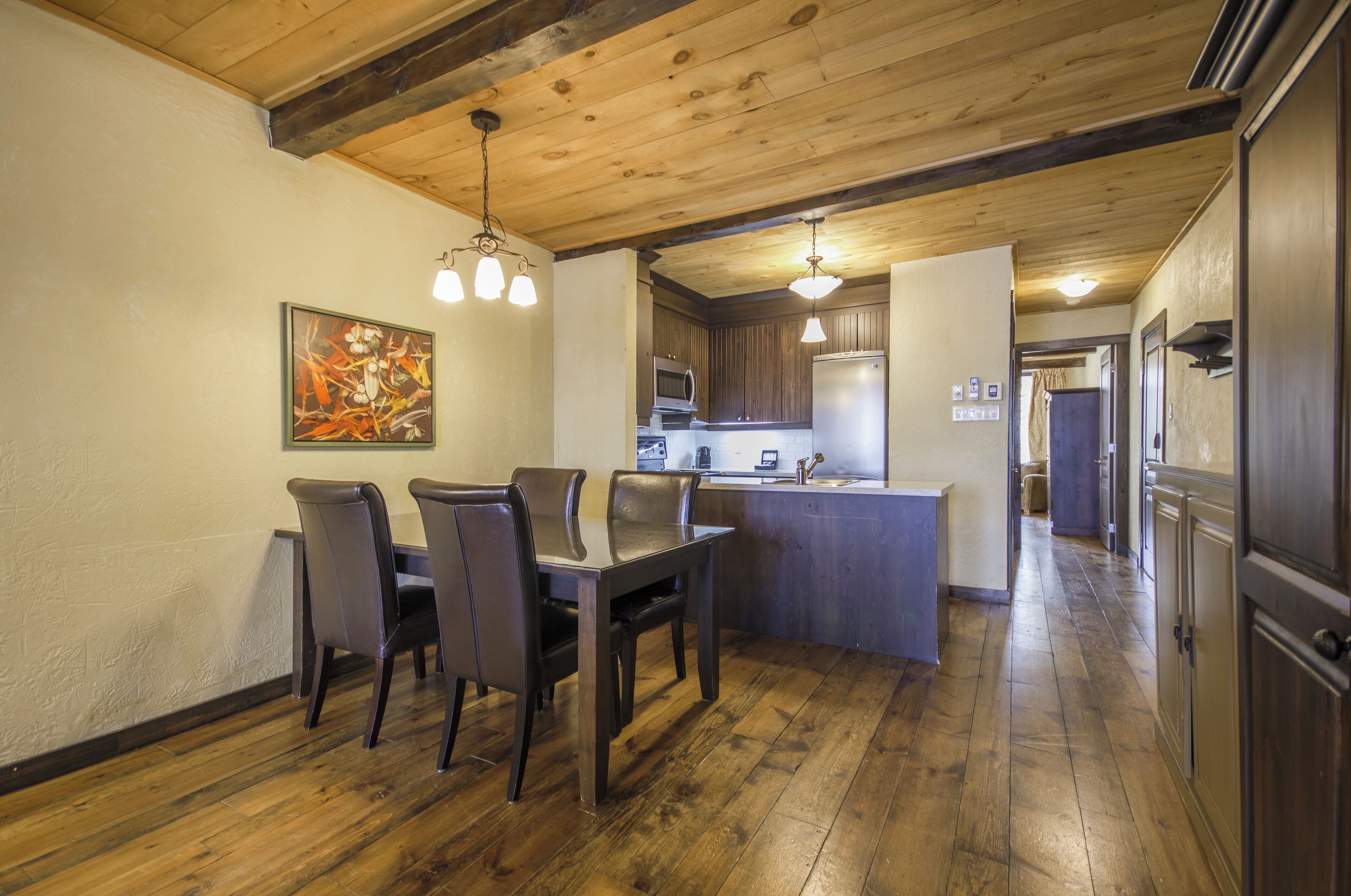 A dining area with a wooden table and chairs, a kitchen with modern appliances, and a wooden ceiling.
