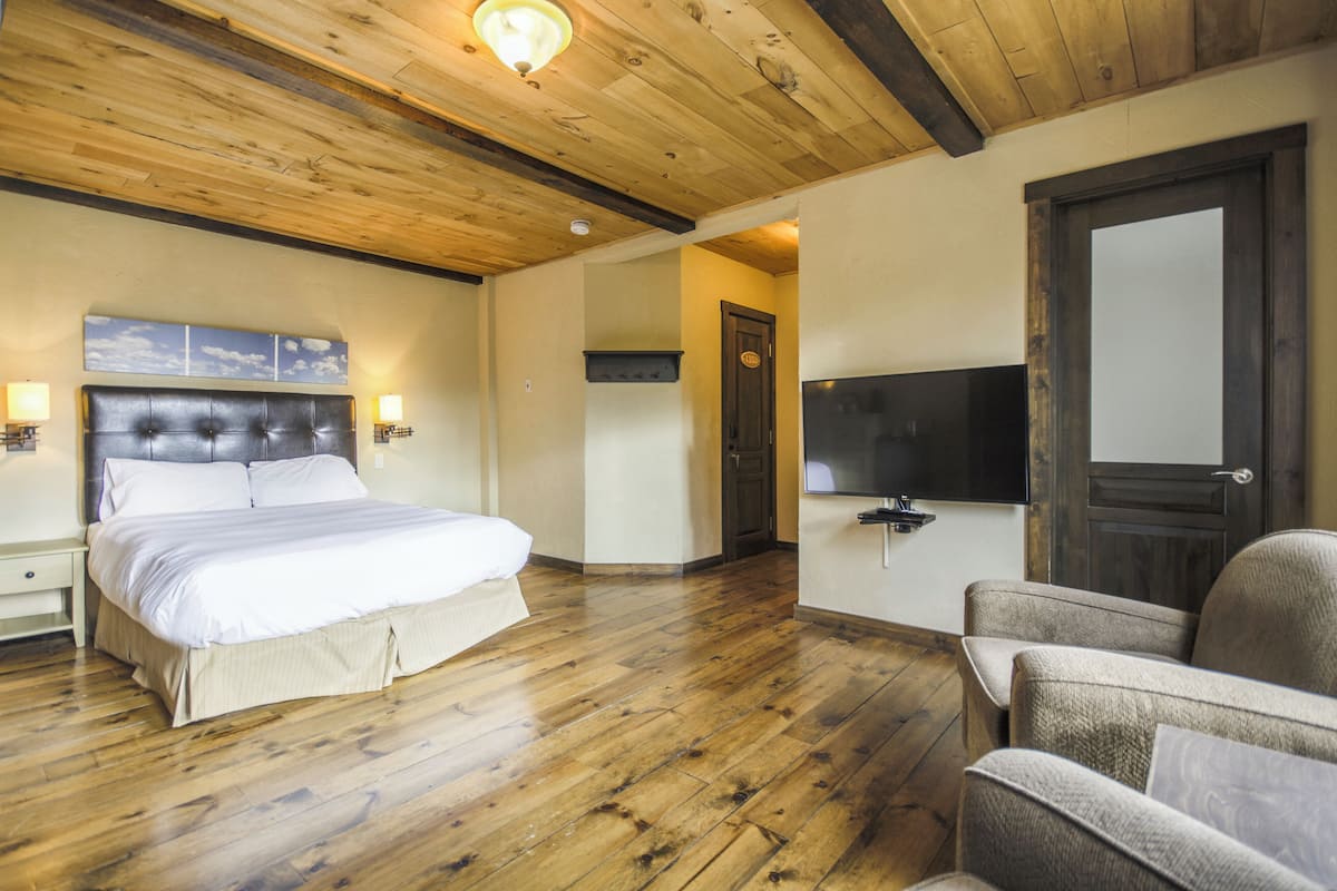 A bedroom with a bed, a chair, a television, and wooden flooring.