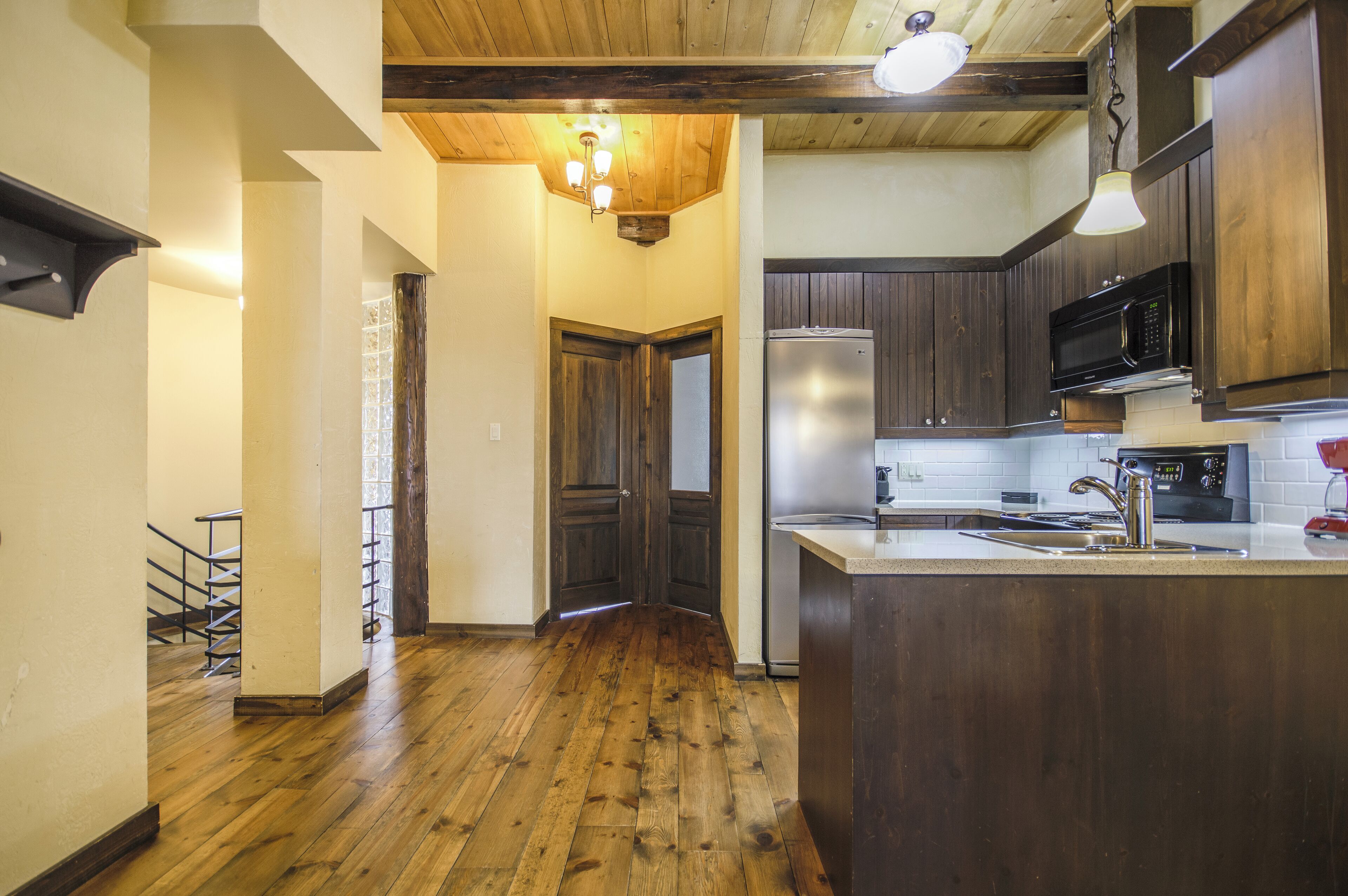 A kitchen with wooden flooring, dark cabinets, a stainless steel refrigerator, and a built-in microwave.