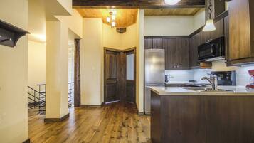 A kitchen with wooden flooring, dark cabinets, a stainless steel refrigerator, and a built-in microwave.